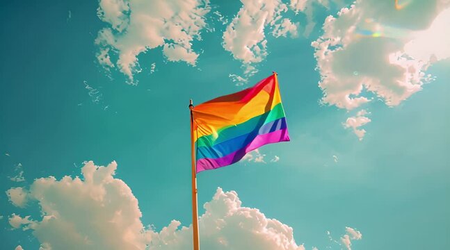 Rainbow Pride Flag Waving in the Sky. Vibrant rainbow flag flutters against a backdrop of blue sky and clouds