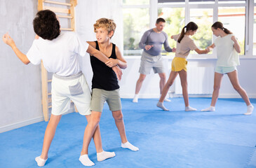 Children in sparring improve skill of performing strangulation and neutralizing enemy during krav maga class. Pupils strike out at mandible and body at self-defense lesson