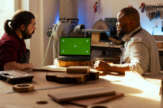 Happy manufacturers using CAD software on isolated screen laptop, debating wood design to use. Smiling carpenters chatting, using program on chroma key notebook to make furniture schematics