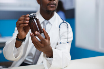 Close-up shot of a black man wearing a lab coat and holding a prescription medicine in the clinic...