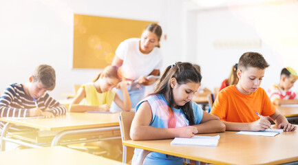 Children sitting at lesson in classroom, teacher standing