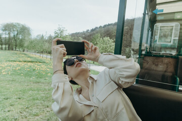 A young girl takes pictures of nature on a smartphone while sitting on a train.