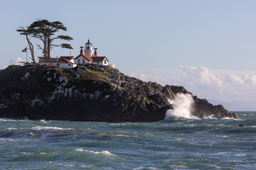 A lighthouse sits on a rocky hillside. The lighthouse is white and red, and it is surrounded by a lush green hillside. The scene is peaceful and serene. Battery Point Lighthouse, California.