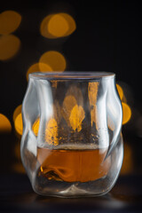 A glass of liquor is sitting on a table. The glass is half full and has a yellowish tint to it. The image has a warm and inviting mood, suggesting that the drink is meant to be enjoyed - 786753017
