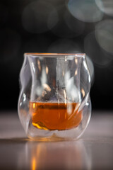 A glass of liquor is sitting on a table. The glass is half full and the liquid inside is brown....