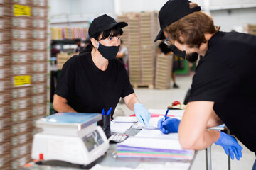 Diligent efficient friendly manager in protective mask invites factory warehouse worker to sign documents.