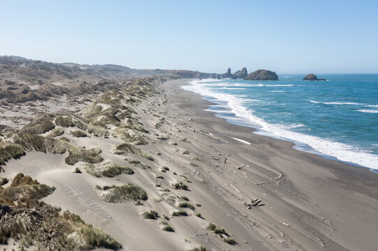 A beach with a rocky shoreline and a body of water. The beach is mostly covered in sand and there are some rocks scattered around. The sky is clear and the sun is shining brightly