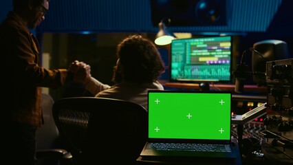 Artist and sound designer working as a team to produce new tracks, greenscreen laptop. Musician and audio technician collaborating on music, mixing on audio console with motorized faders. Camera B.