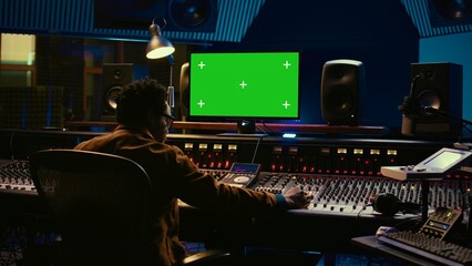 African american music producer working with greenscreen on pc, using mixing console to do mix and...