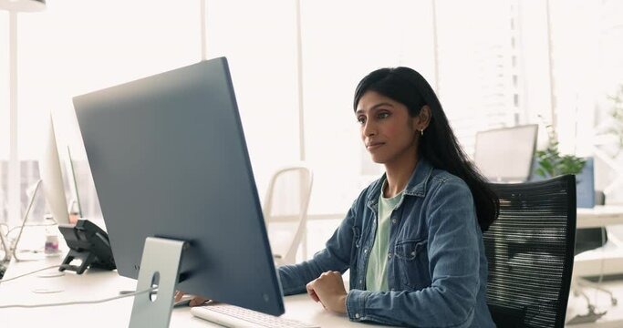 Serious focused Indian woman, employee sitting at shared desk in coworking working on PC, prepare report, respond to emails, conducting research, writing documents, create presentation, manage project