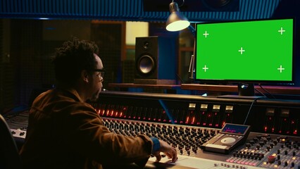 African american sound designer looks at greenscreen to record and edit tunes, uses mixing console...
