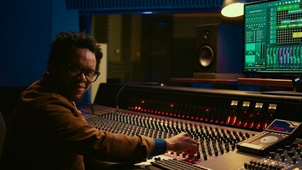 Portrait of african american sound designer mixing and mastering tracks with professional audio...