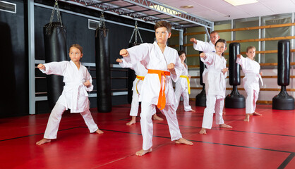 Group of preteen boys and girls doing karate kicks with male coach during karate class © JackF