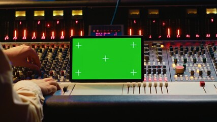 Audio expert mixing and mastering tunes on editing software next to greenscreen tablet, producing...