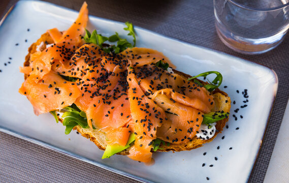 Healthy toast with smoked salmon and ripe avocado garnished with fresh greens and sesame seeds