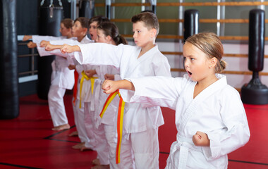 Group of young girls and boys in kimono doing kata in gym.
