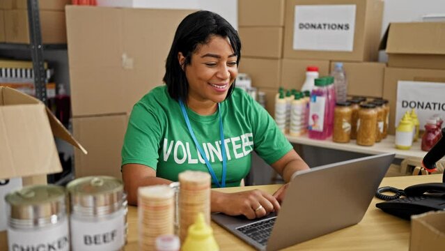 Hispanic woman volunteering at indoor donation center, organizing supplies with laptop
