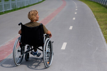 Obraz premium Rear view of an elderly woman in a wheelchair riding on a bike path. 