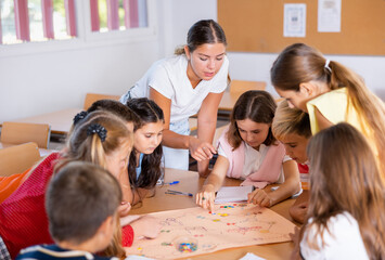 Happy preteen children and female teacher playing together educational board game in classroom at elementary school