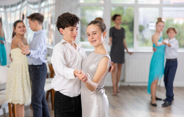 Happy interested teenage students preparing for college festive event, rehearsing ballroom dance steps in spacious classroom while female teacher observing from background.. - obrazy, fototapety, plakaty