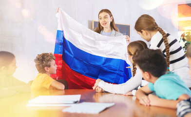 Smiling young female teacher conducting lesson for preteens, showing state flag of in audience of...