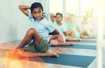 Young african boy in group of multiethnic children doing yoga on mat in studio