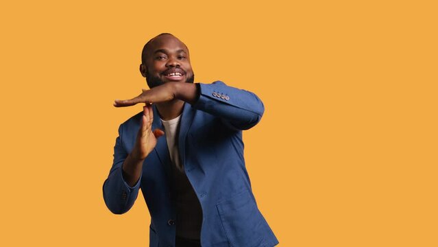 Cheerful african american man asking for timeout, doing hand gestures, halting activities. Friendly upbeat person doing pause sign gesturing, wishing for break, studio background, camera B