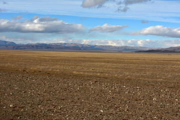 A huge flat steppe with dried grass at the foot of a high mountain range under a cloudy sky on an autumn day.