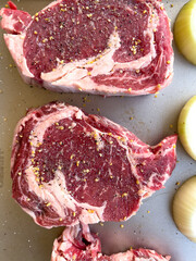 Raw Ribeye Steaks Seasoned with Spices and Onion Halves on Tray