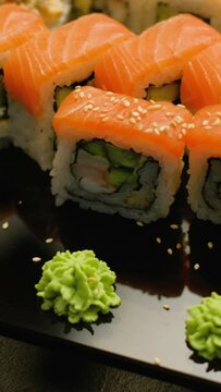 Vertical video. Tasty sushi. Japanese food. Salmon rolls set assortment decorated with sesame in restaurant on dark background.