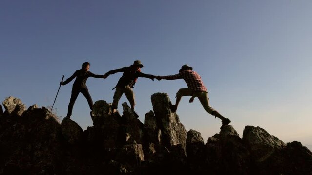 Silhouette of Group team tourists lends helping hand climb cliffs mountains helping hand. teamwork people climbers climb top overcoming hardships, teamwork helping hand business travel  concept.