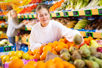 Young european girl purchaser choosing oranges in a grocery store