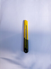 yellow and black paper cutter knife, small knife, blade, exacto knife, paper cutter on white background, dappled sunlight