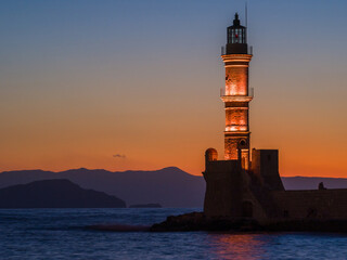 Illuminated old lighthouse in a port town at evening (Chania, Crete, Greece)