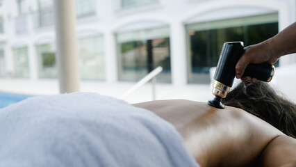 Fascial massage gun massage. Woman enjoy relax treatment in luxury spa by poolside
