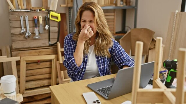 Disgusted young latin beauty sitting at carpentry table, holding nose against intolerable stinky smell, face expressing revulsion