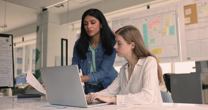 Two women colleagues engaged in teamwork in office, using laptop, make sales analysis, review report, charts and graphs, brainstorming solutions, making decisions based on data, prepare presentations