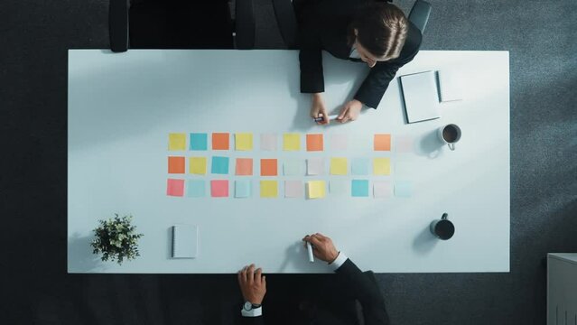 Top view of professional business people making agreement and brainstorm marketing idea or plan by using colorful sticky notes on table with coffee and paper placed on at meeting room. Directorate.