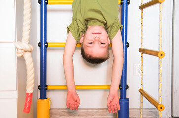 Child hangs upside down on horizontal bar at home. Happy boy swinging upside down on playground. Child playing on horizontal bar.