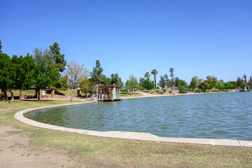Grassy curved shores with some distant shady trees around water surface of Kiwanis park lake, Tempe, Arizona; copyspace