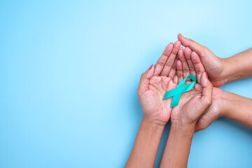 Ovarian Cancer Month, Cervical Cancer Day. Close-up Teal Awareness Ribbon on People Hands to Support Cancer Survivor.