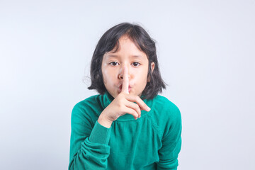 Beautiful Asian little girl putting finger up to lips and ask silence on yellow background