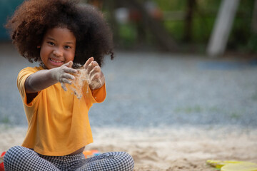 African child girl happy playing with sand in the playground, she let the sand slipping through her...