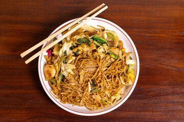 Fried noodle with chicken and vegetables in a white bowl on a wooden table. After edits.