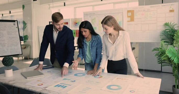 In boardroom group of businesspeople gathers around conference table, review charts and graphs data, do market analysis, planning marketing strategy, learn revenue, profit, cash flow, financial ratio