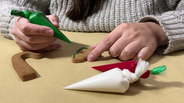 4K video. Woman paints gingerbread tree in shape of Christmas tree on craft table surface. Female hands hold plastic bag with green paint. Preparation for winter holiday concept. Happy New Year 2025