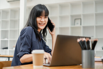 Happy businesswoman in navy shirt talking on the phone with a laptop and coffee cup on the desk.