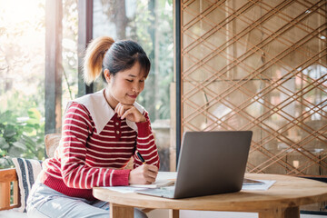 Woman in a striped red sweater and light jeans working on her laptop at a wooden table.