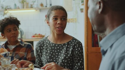 African American teen girl smiling and talking with dad over meal during family dinner at home. Over the shoulder view