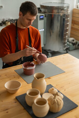 Potter paints ceramic dishes with a brush. Vertical photo.